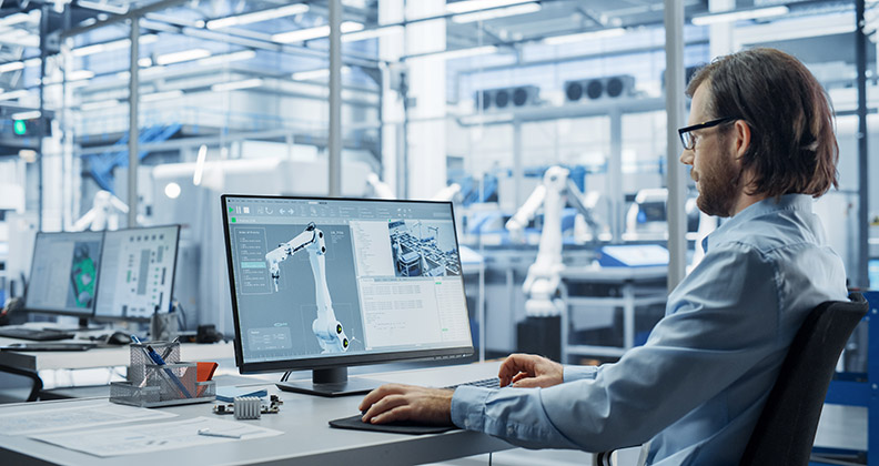 Engineer sitting at a computer looking at a robot arm on the screen