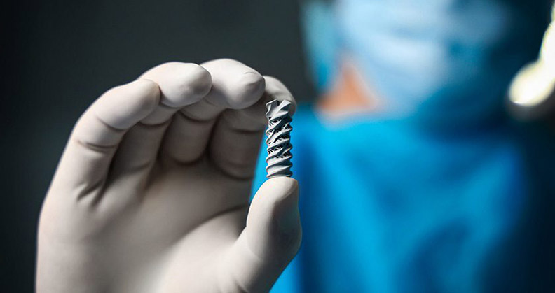 Close up of a gloved surgeon hand holding Spinal Simplicity's Patriot-SI implant