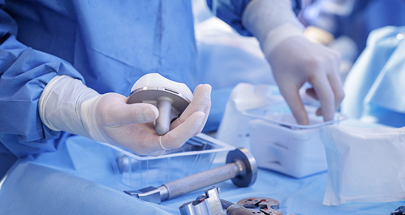 gloved surgeon hand holding a knee implant near the back table of an O.R.