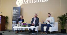 Panelists sitting in white chairs on a dais at OMTEC