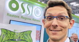 Orahn Preiss-Bloom smiling at a conference in front of an OSSIO banner