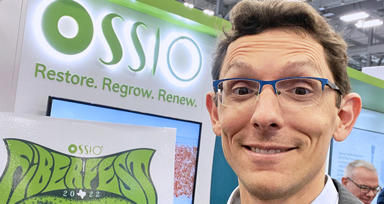Orahn Preiss-Bloom smiling at a conference in front of an OSSIO banner