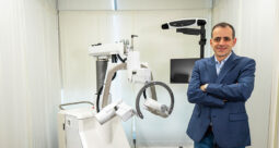Mohammad Abedin-Nasab, Ph.D., standing with arms folded in front of the Robossis, a new trauma robot